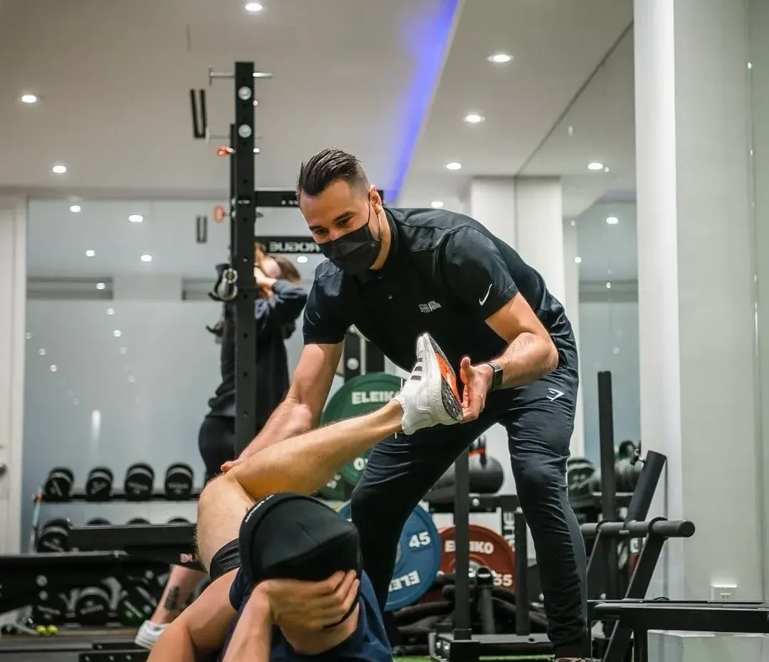 Roman supporting a client through a floor-based exercise in a strength gym