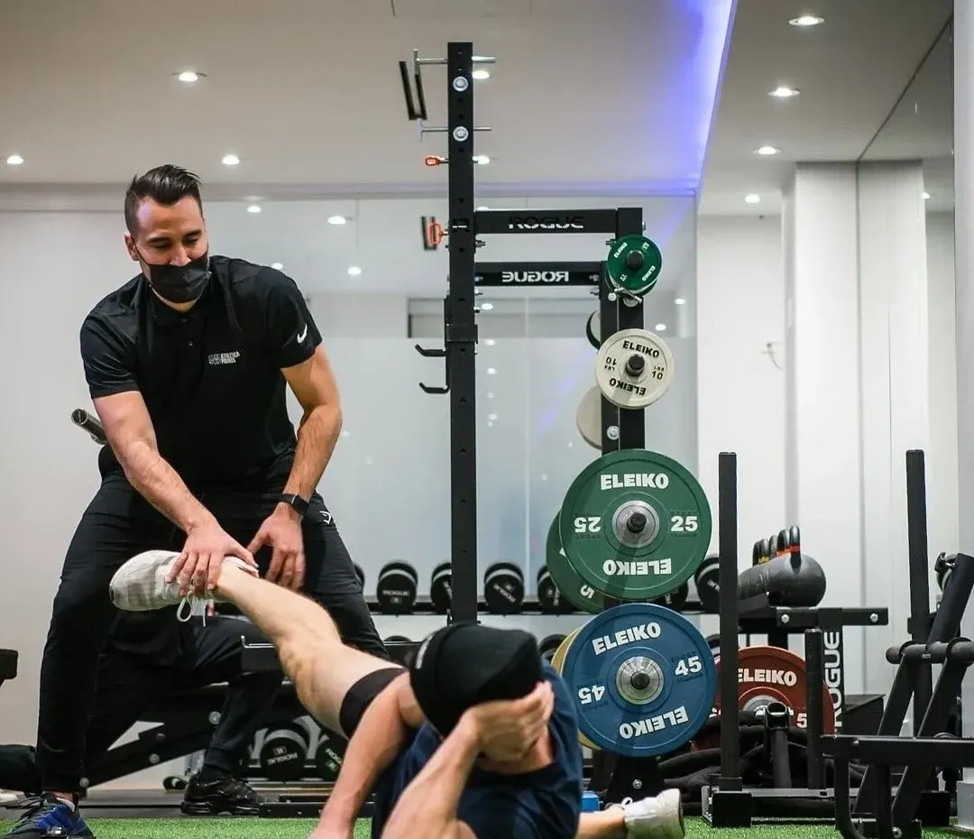 Roman guiding a hamstring stretch on the gym floor at Push Pounds